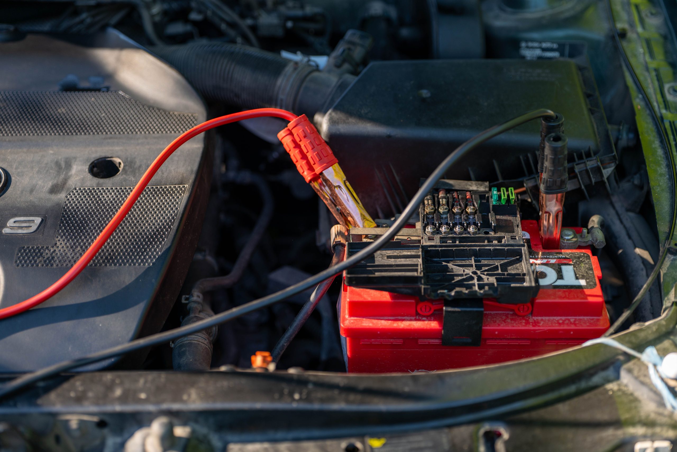 Services Close-up of a car battery with attached jumper cables in an engine bay.